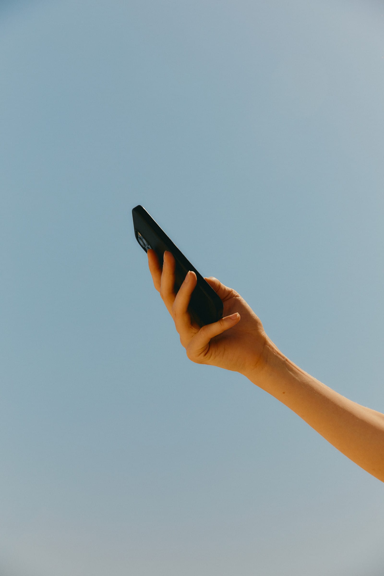 Mano sosteniendo un teléfono contra el cielo azul